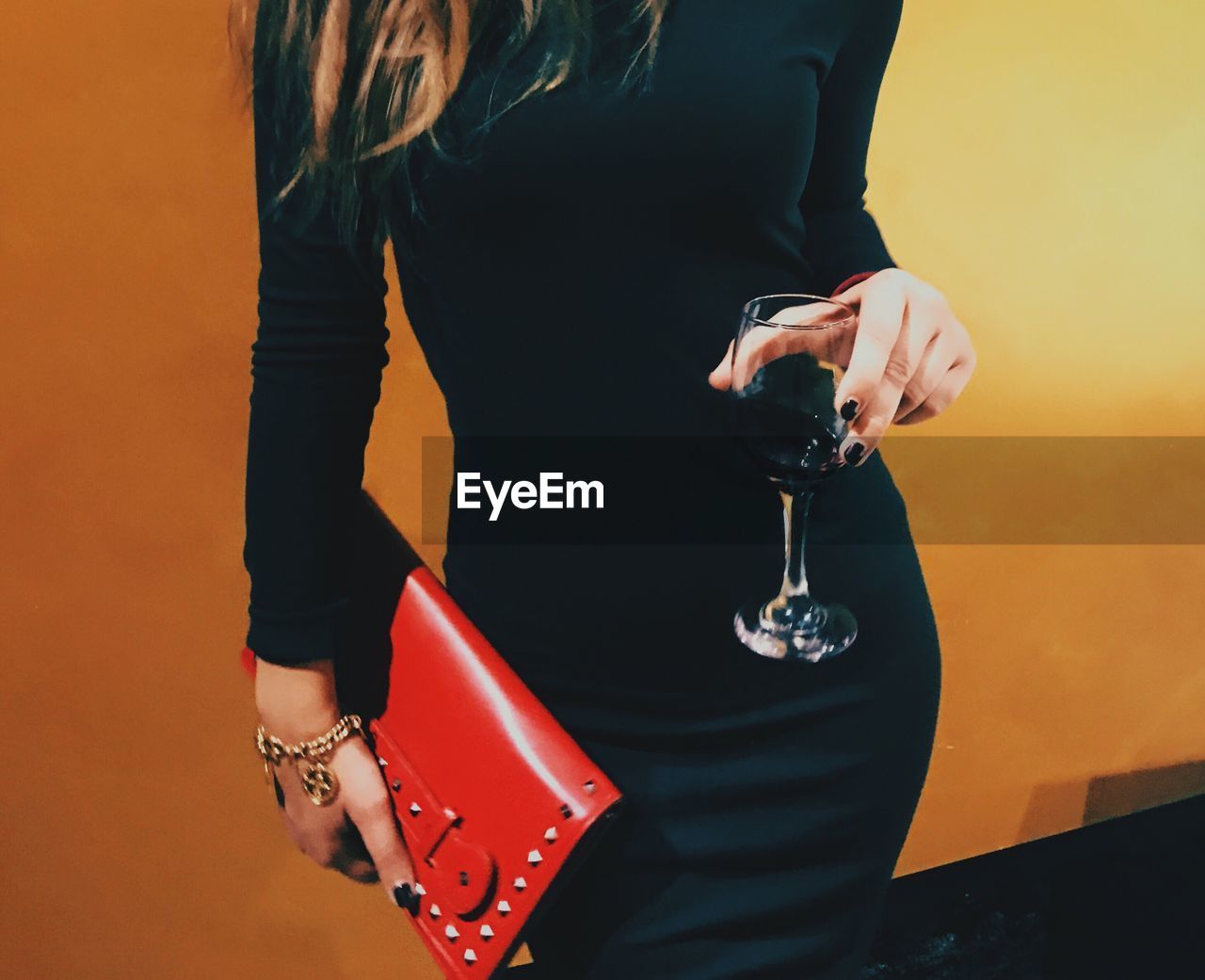Midsection of woman holding wineglass and purse while standing against wall
