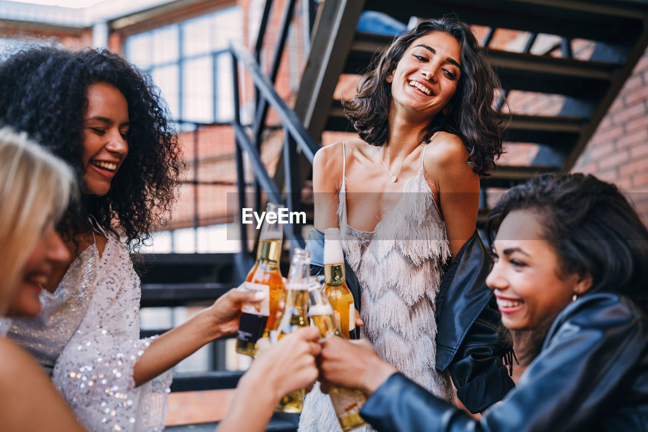 Smiling friends holding beer bottle against staircase