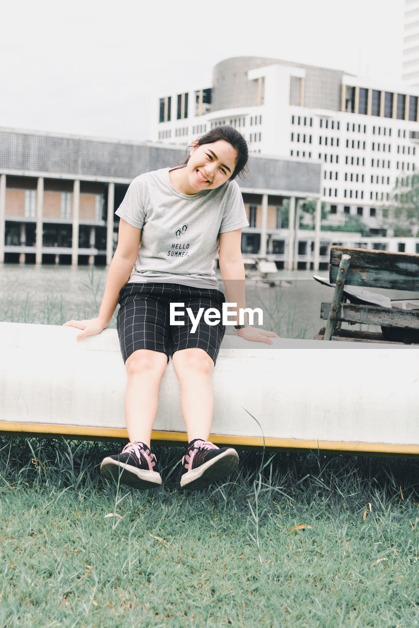 Smiling woman sitting on retaining wall outdoors in city