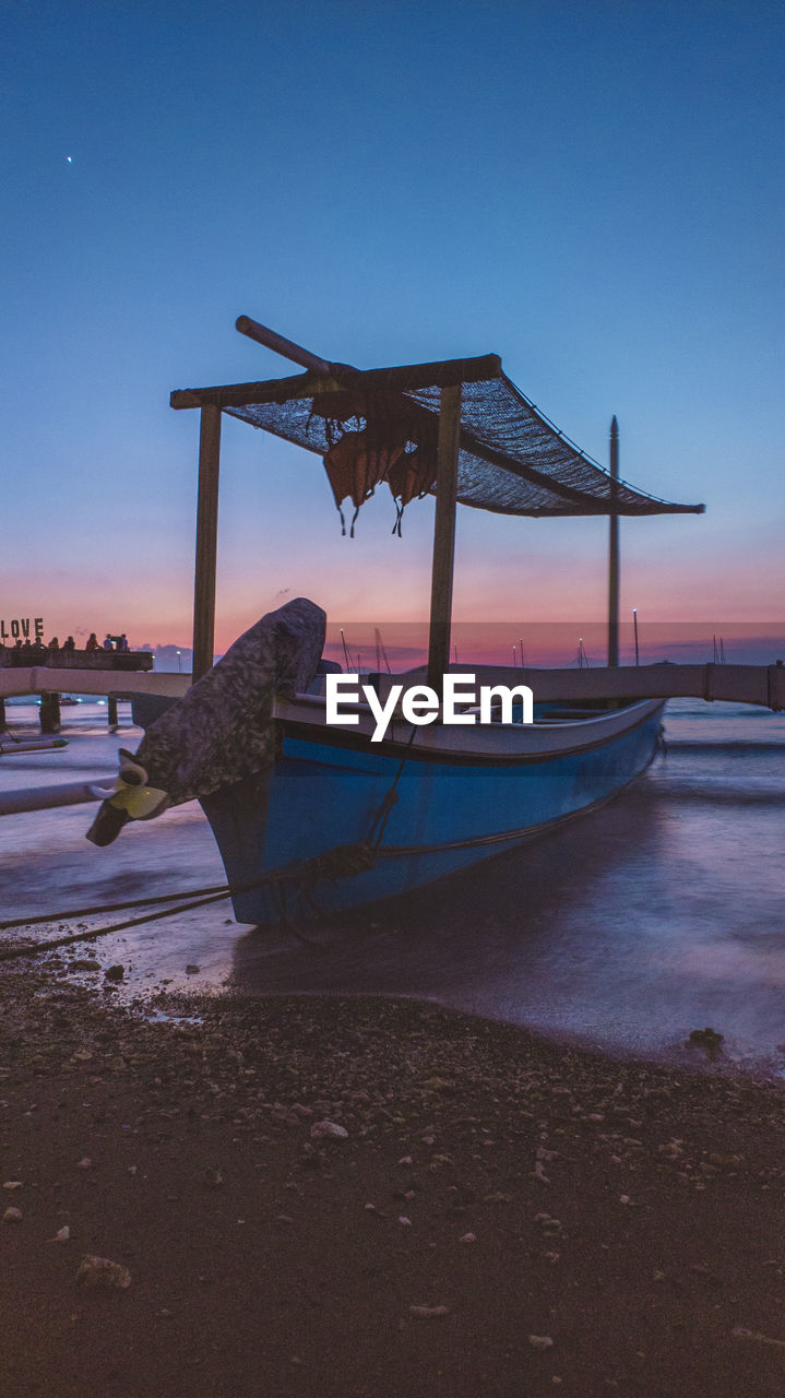 Boat moored on beach against sky during sunset