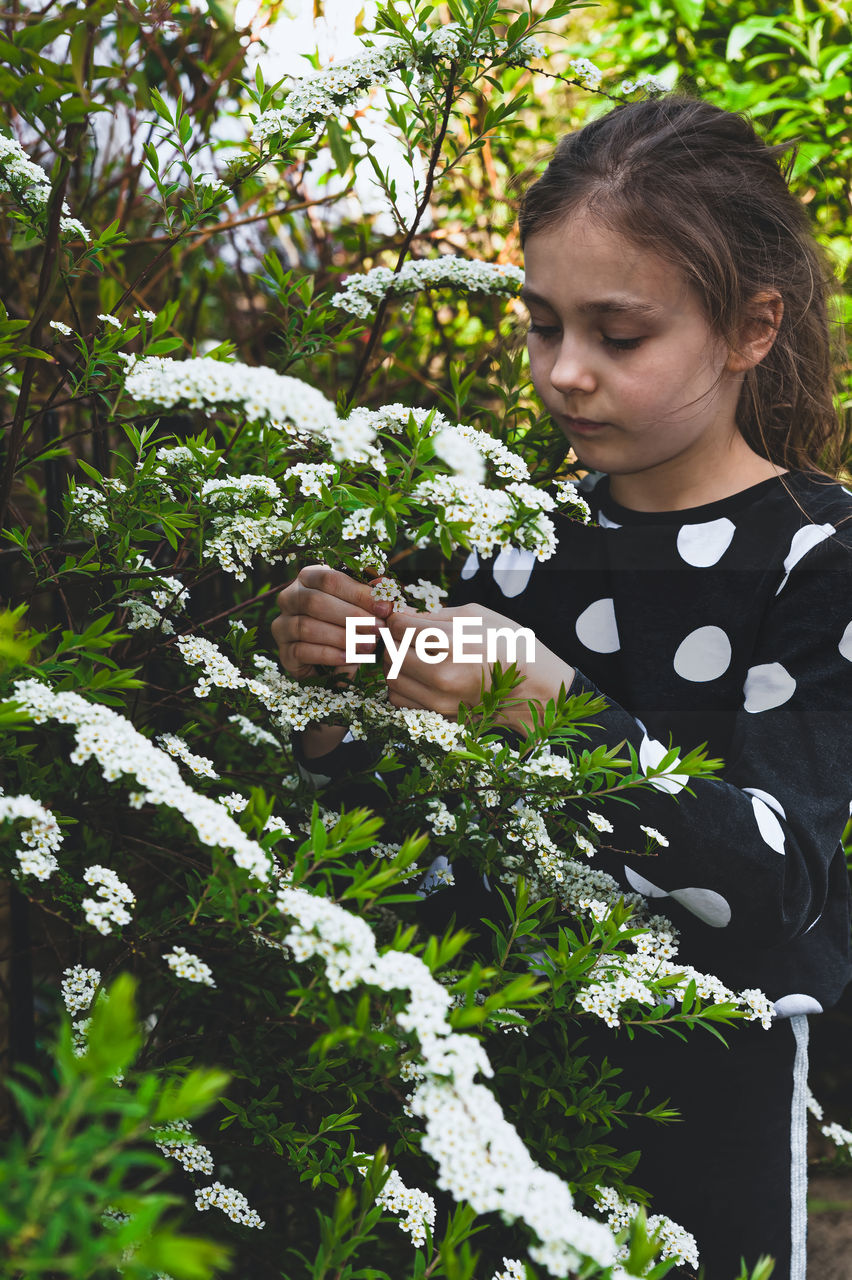 Cute girl holding flowering plant while standing outdoors