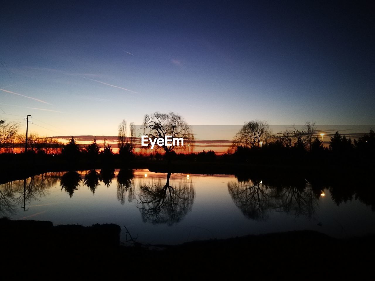 Silhouette trees by lake against sky during sunset