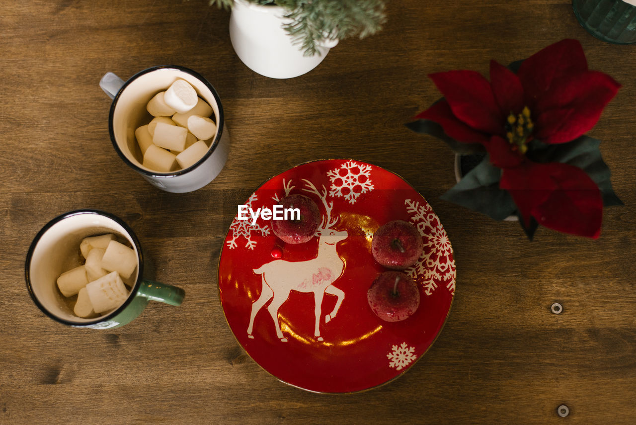 Red chrismas plate with sugar apples, mugs with marshmallows. top view