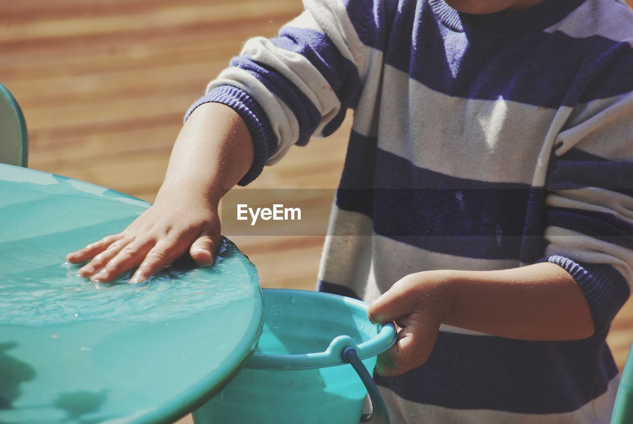 Midsection of boy filling water in bucket