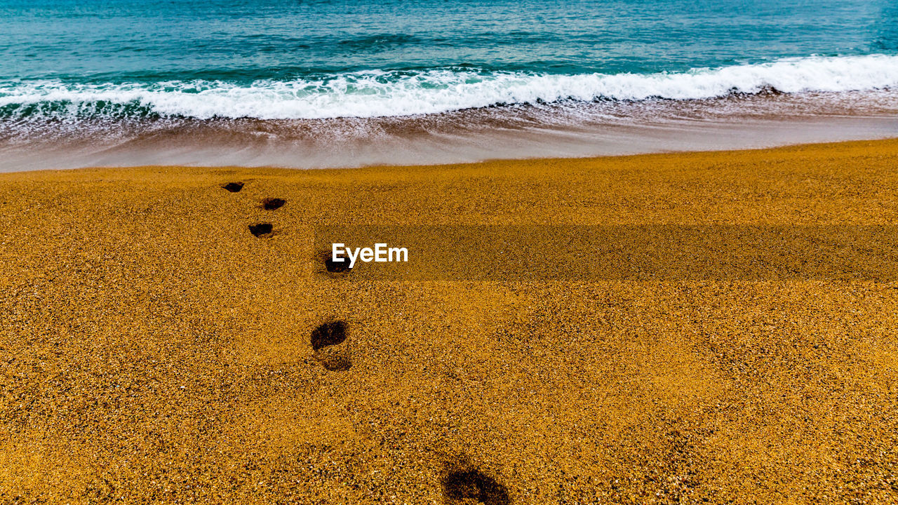 View of the beach with footsteps in the sand against the sea, heading to the water