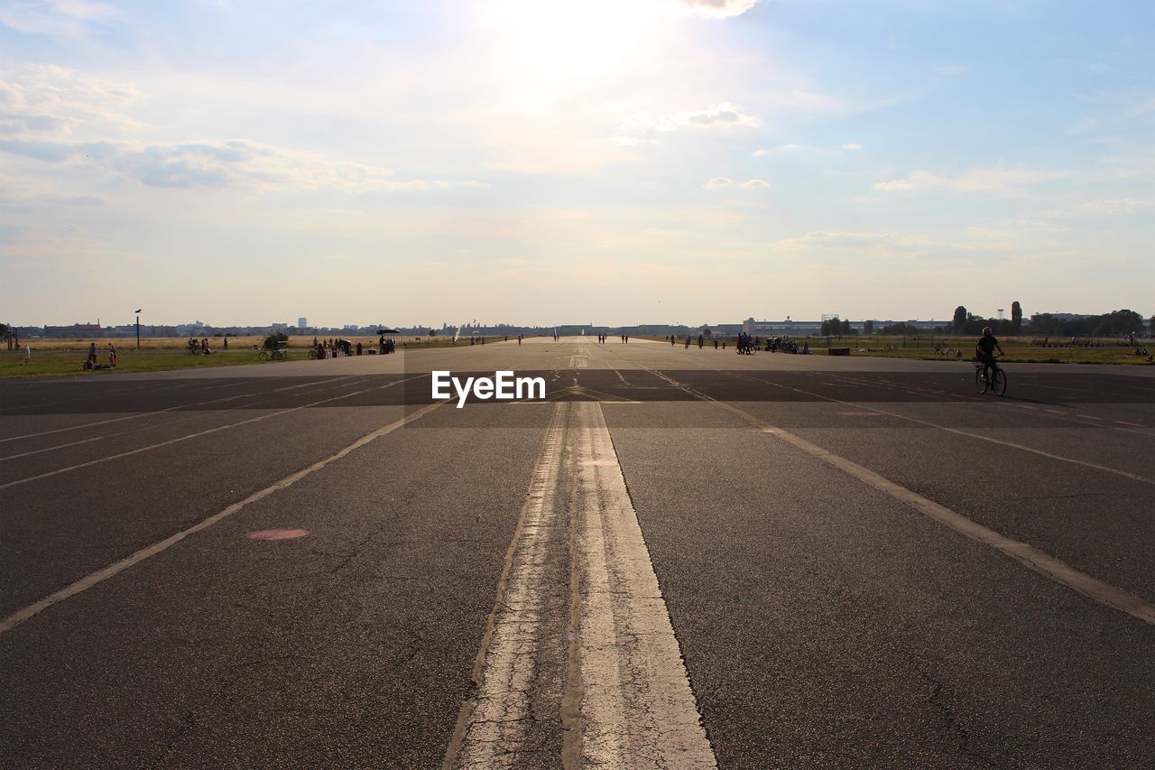 Man riding bicycle on airport runway against sky