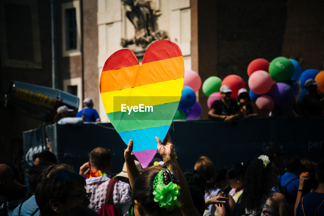 Man holding heart shape rainbow flag amidst people during gay pride parade