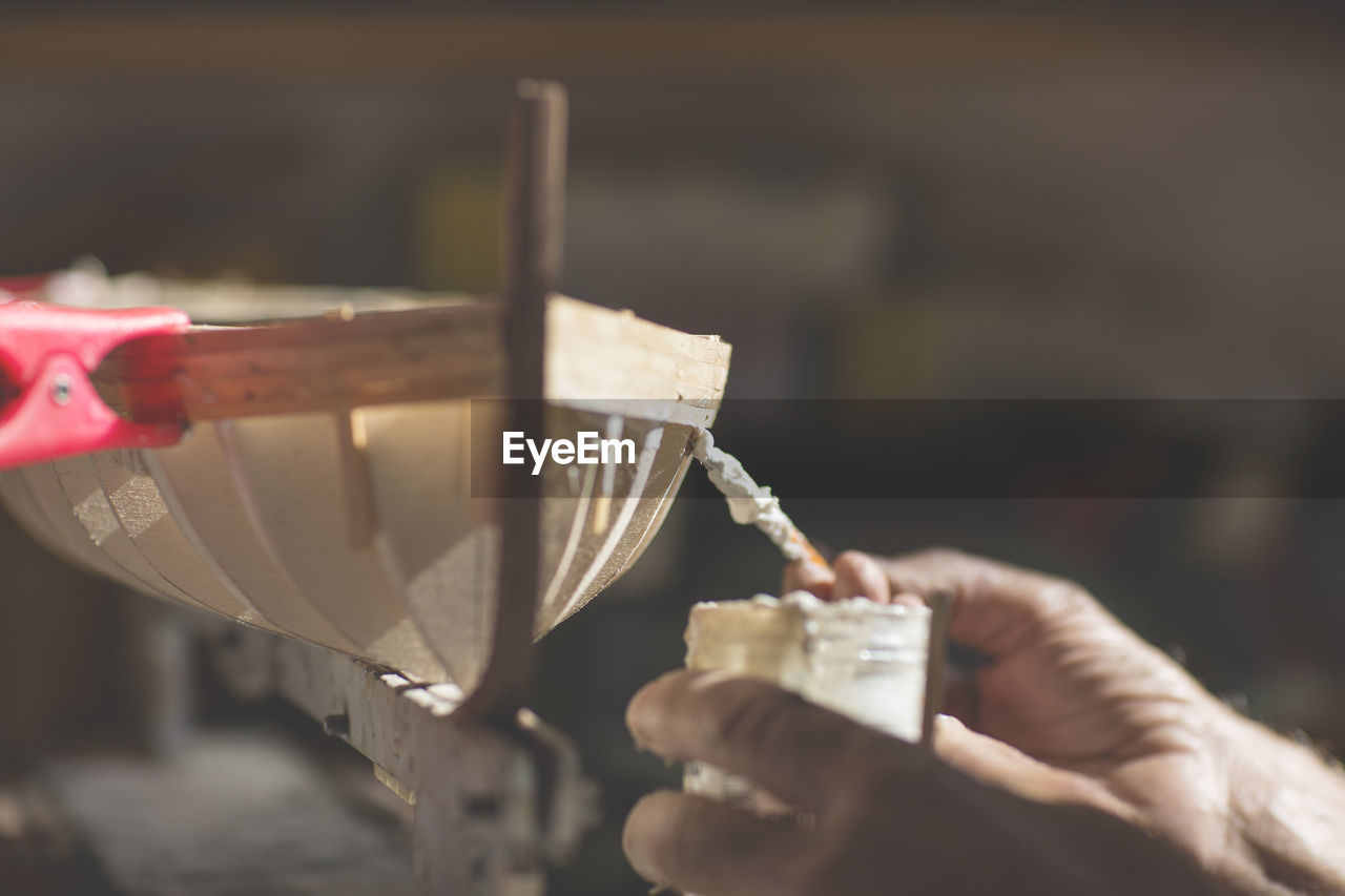 Cropped hands of man making wooden model boat at workshop