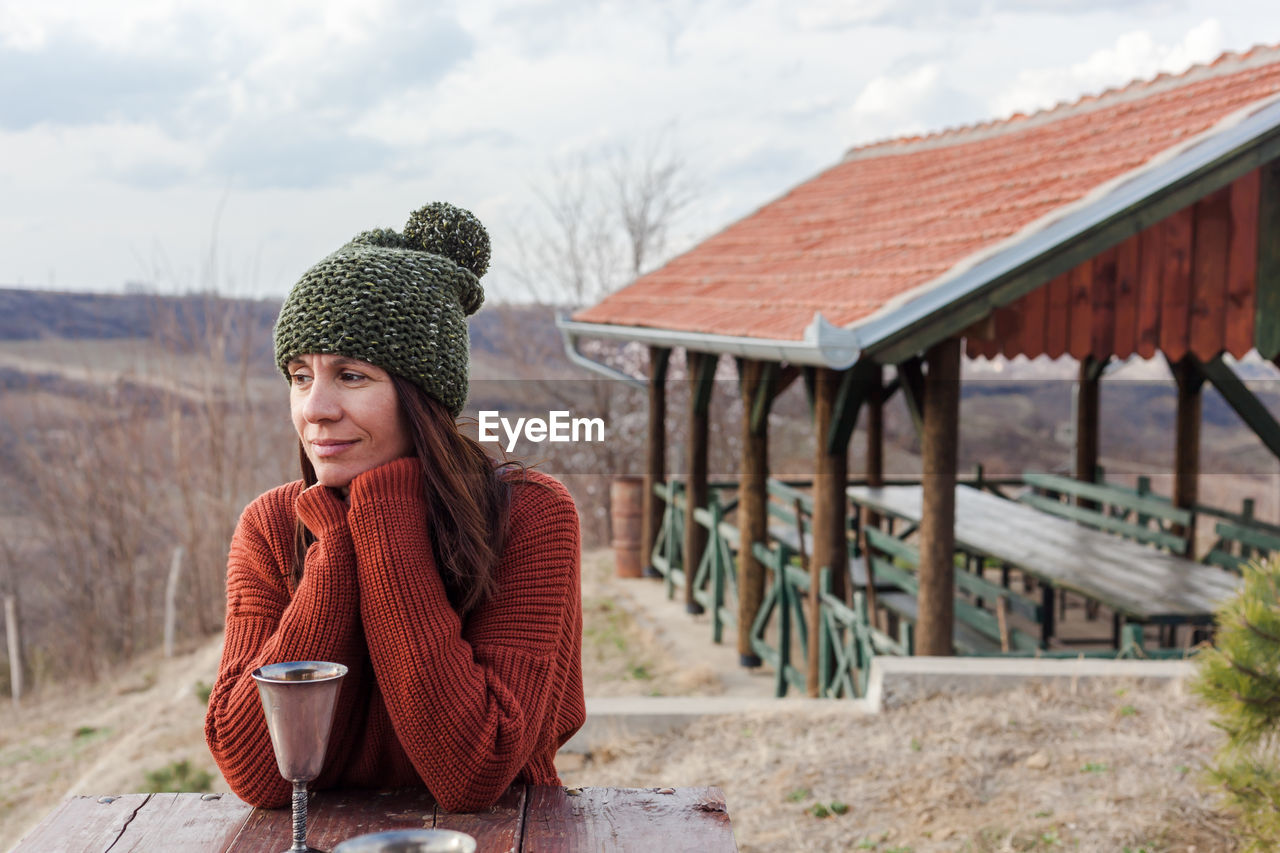 Smiling woman looking away with drink in container on table during winter