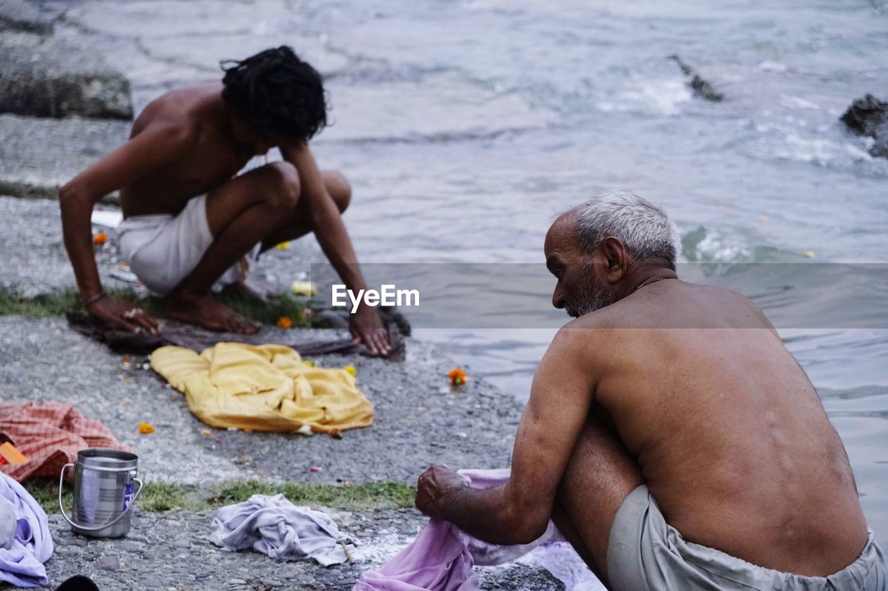 REAR VIEW OF MEN SITTING AT BEACH