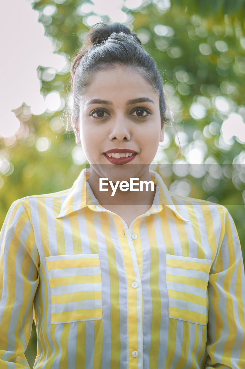 Portrait of smiling young woman against tree