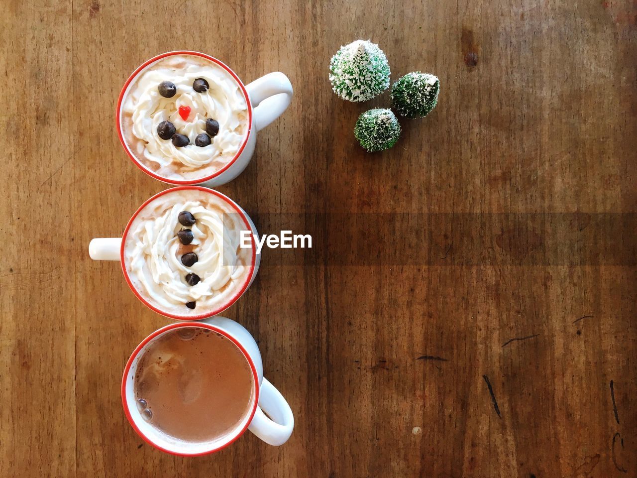 Directly above shot of frothy coffee in cups by artificial christmas tree on wooden table