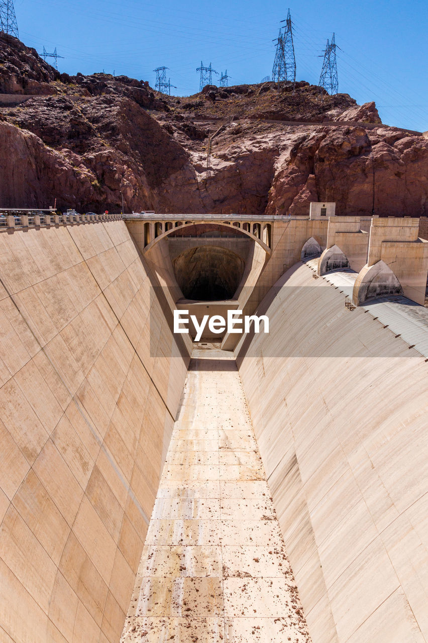 Electricity pylons on rock formation at hoover dam against sky