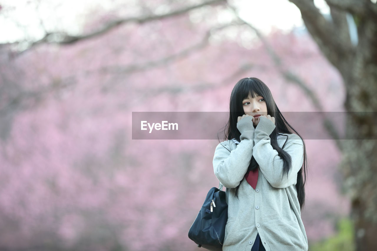 WOMAN STANDING BY PINK FLOWER TREE IN WINTER