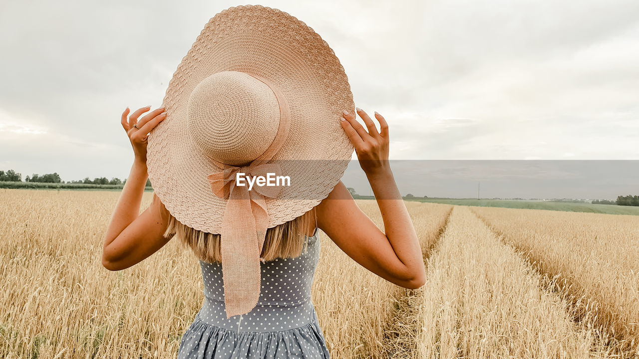 Rear view of woman wearing hat standing on landscape against sky