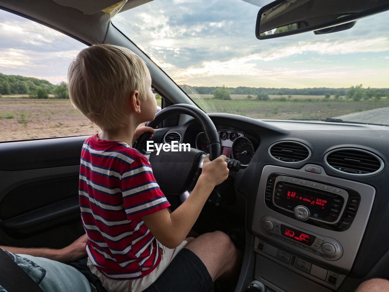 Little caucasian boy drives a car sitting on his daddy's lap