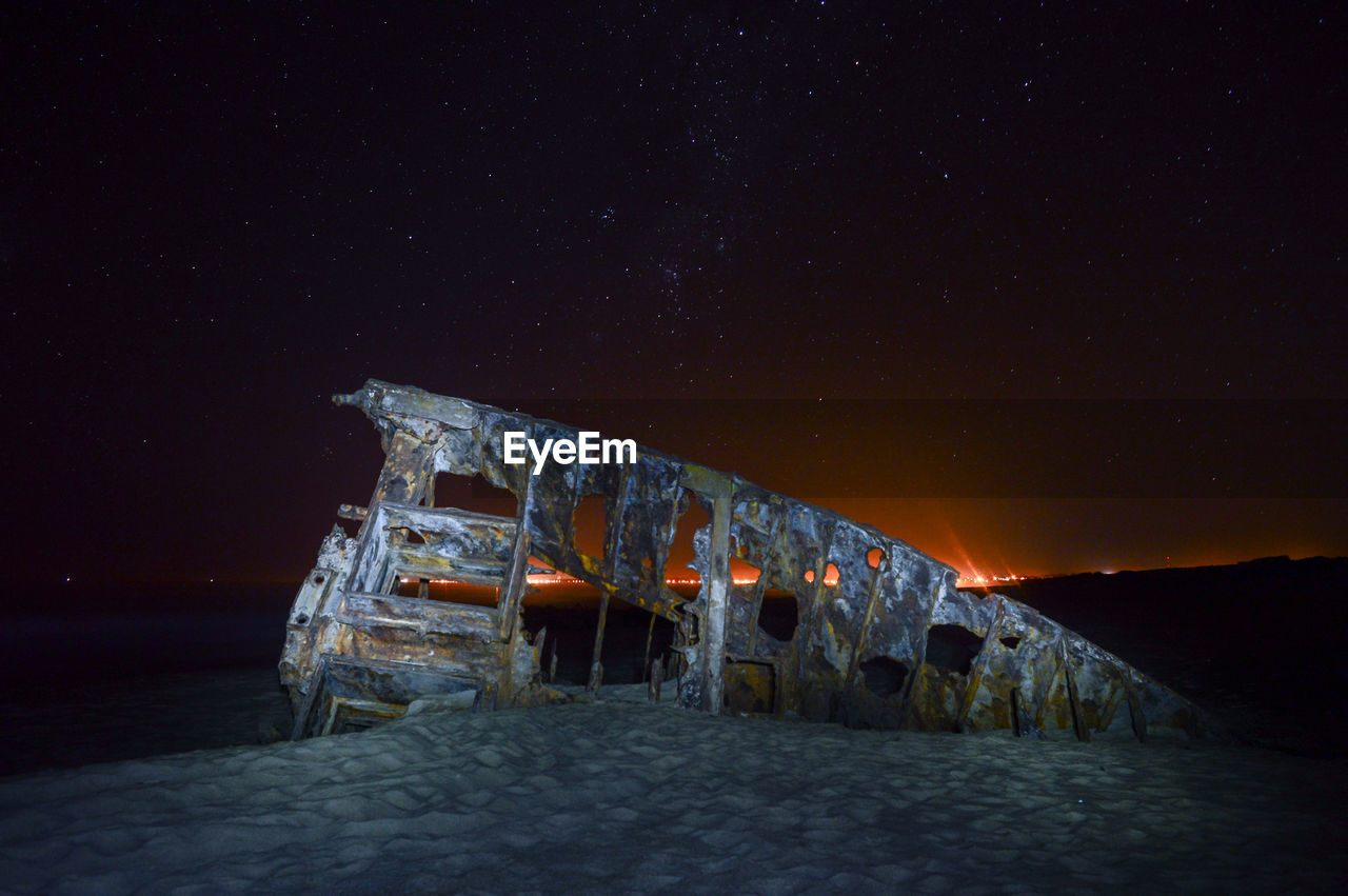 Shipwreck at beach against sky during night