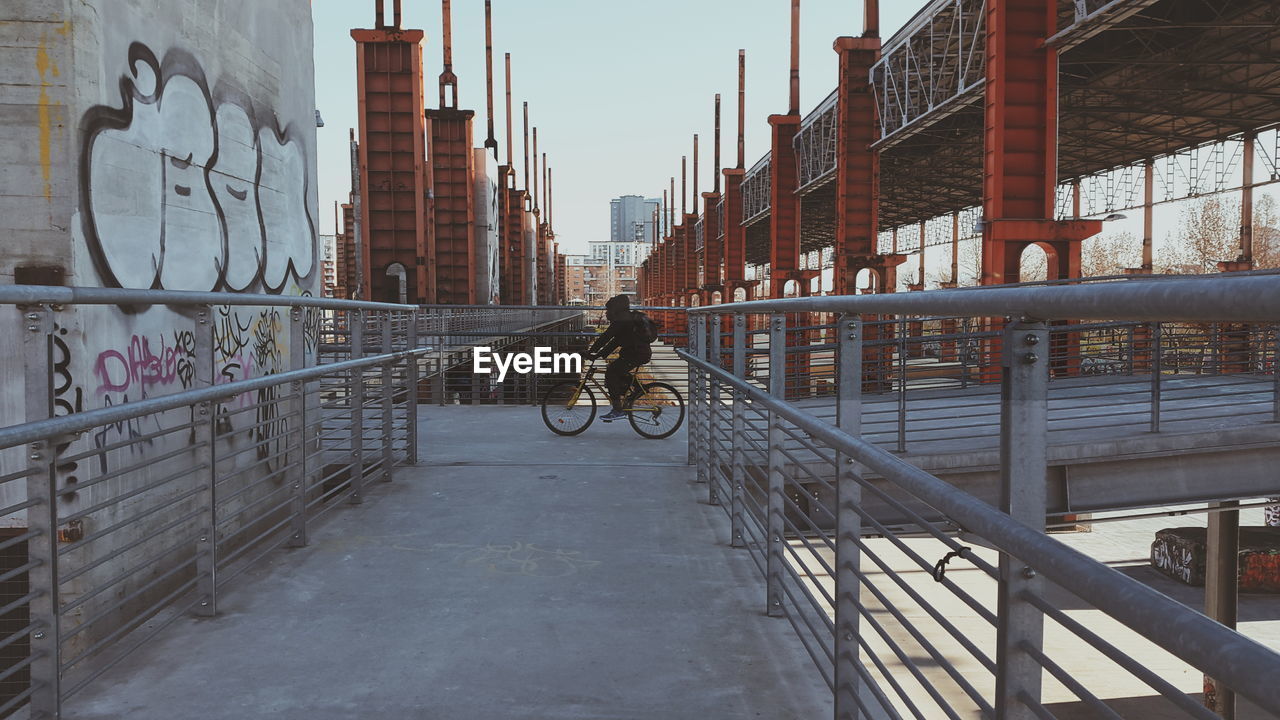 Side view of man riding bicycle on bridge against clear sky