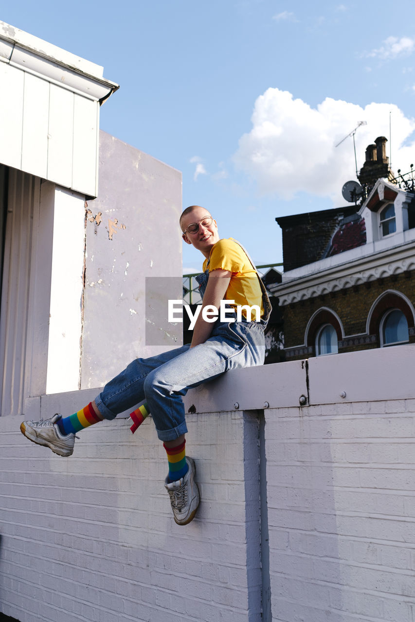 Smiling androgynous person sitting on wall