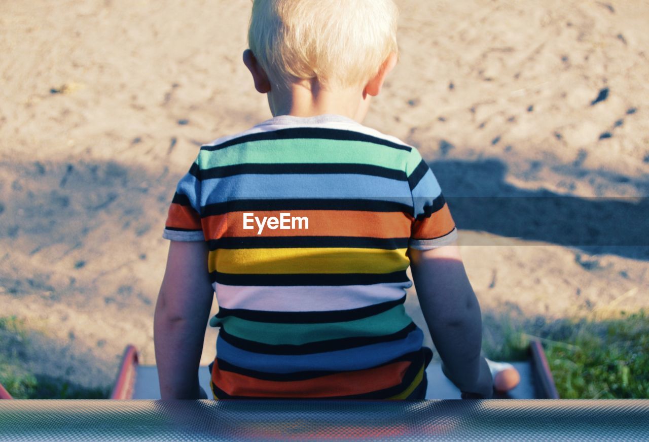 Rear view of boy sitting on slide at playground