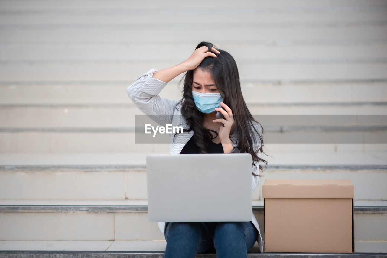 Woman using laptop by box on staircase