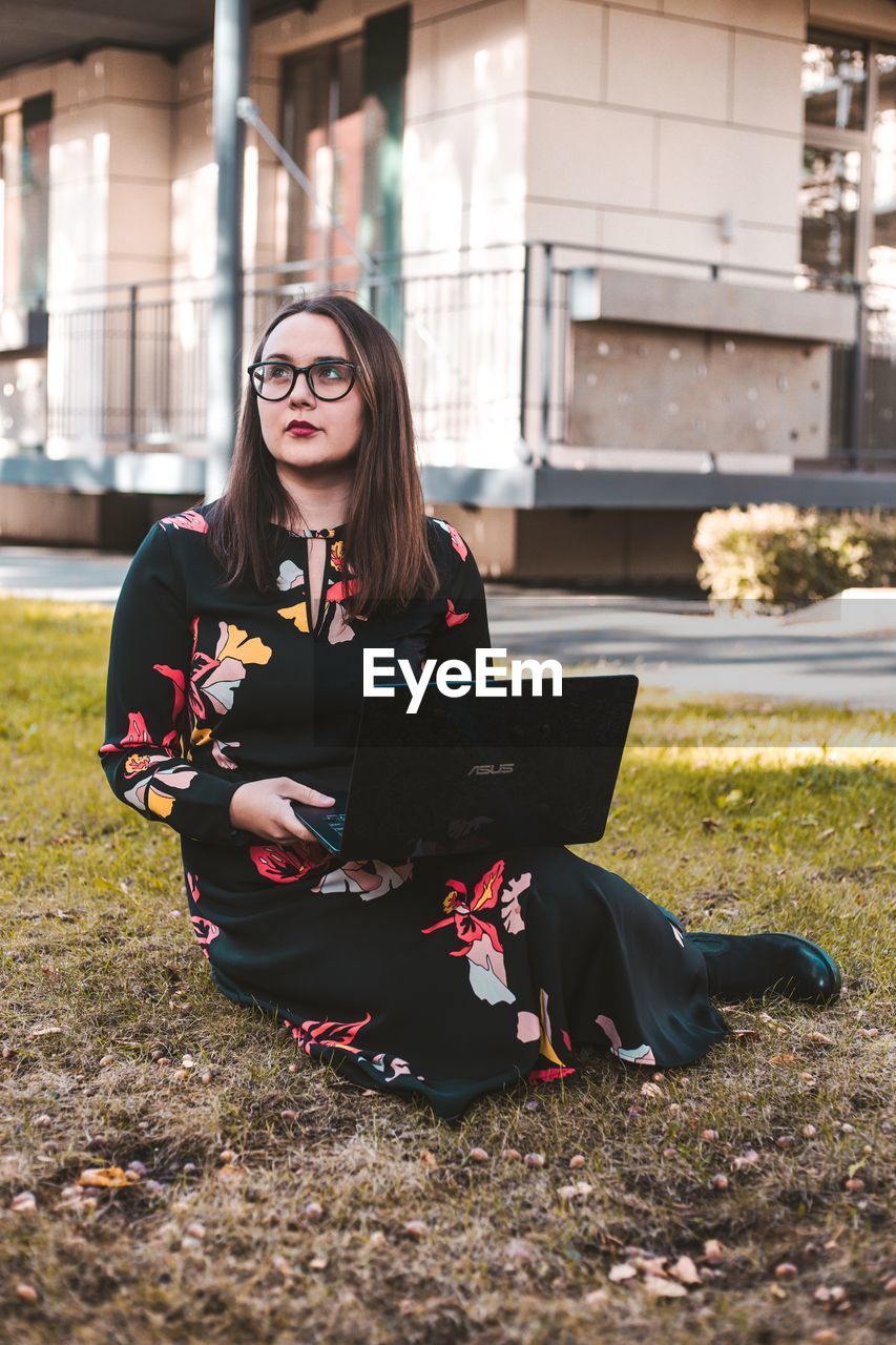 Thoughtful young woman using laptop while sitting on field