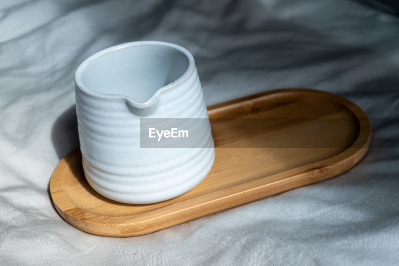 Mug made of white clay or ceramic mug on the wooden plate. subject on the cloth background