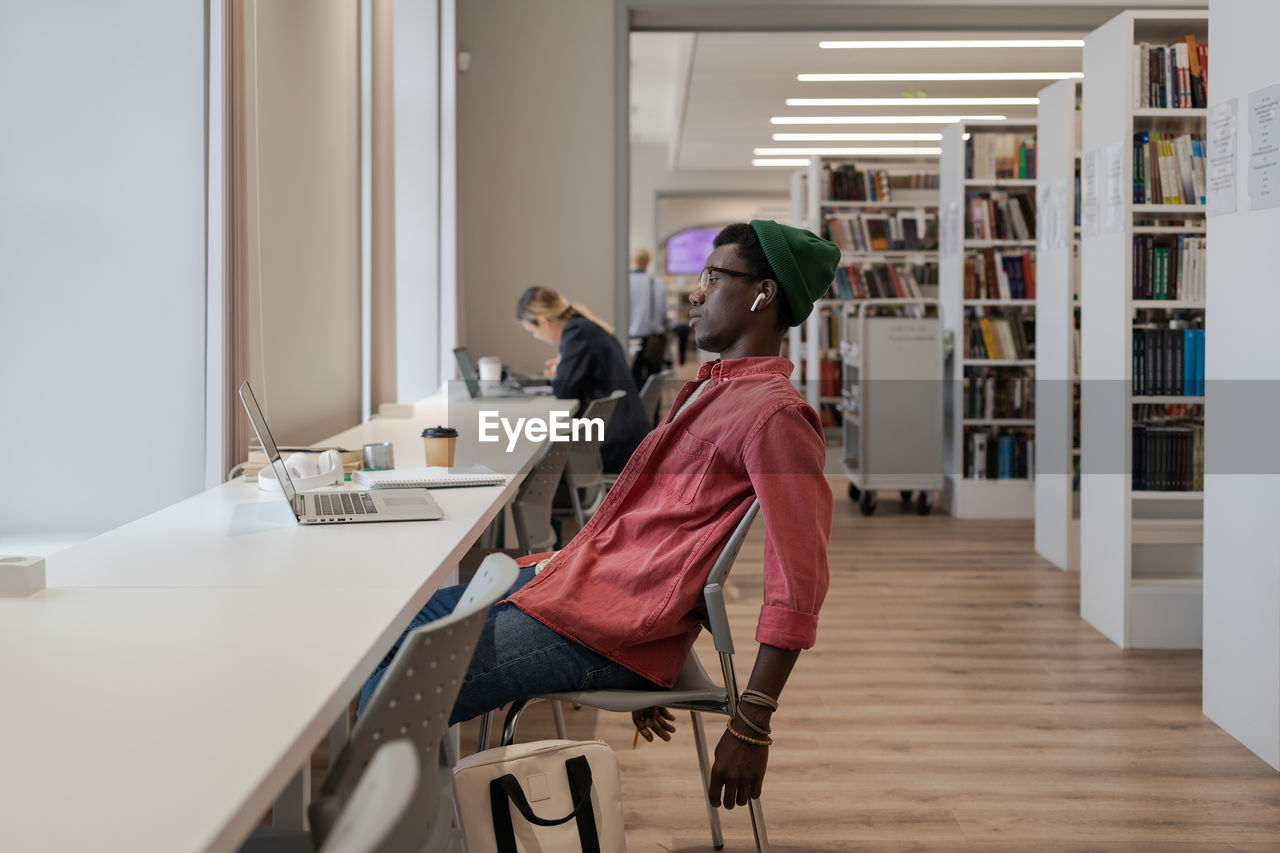 Unhappy black guy student feeling overwhelmed with study while studying online in library