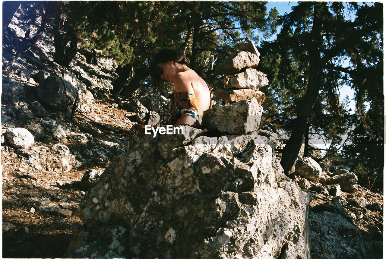 MAN STANDING ON ROCK AGAINST TREE