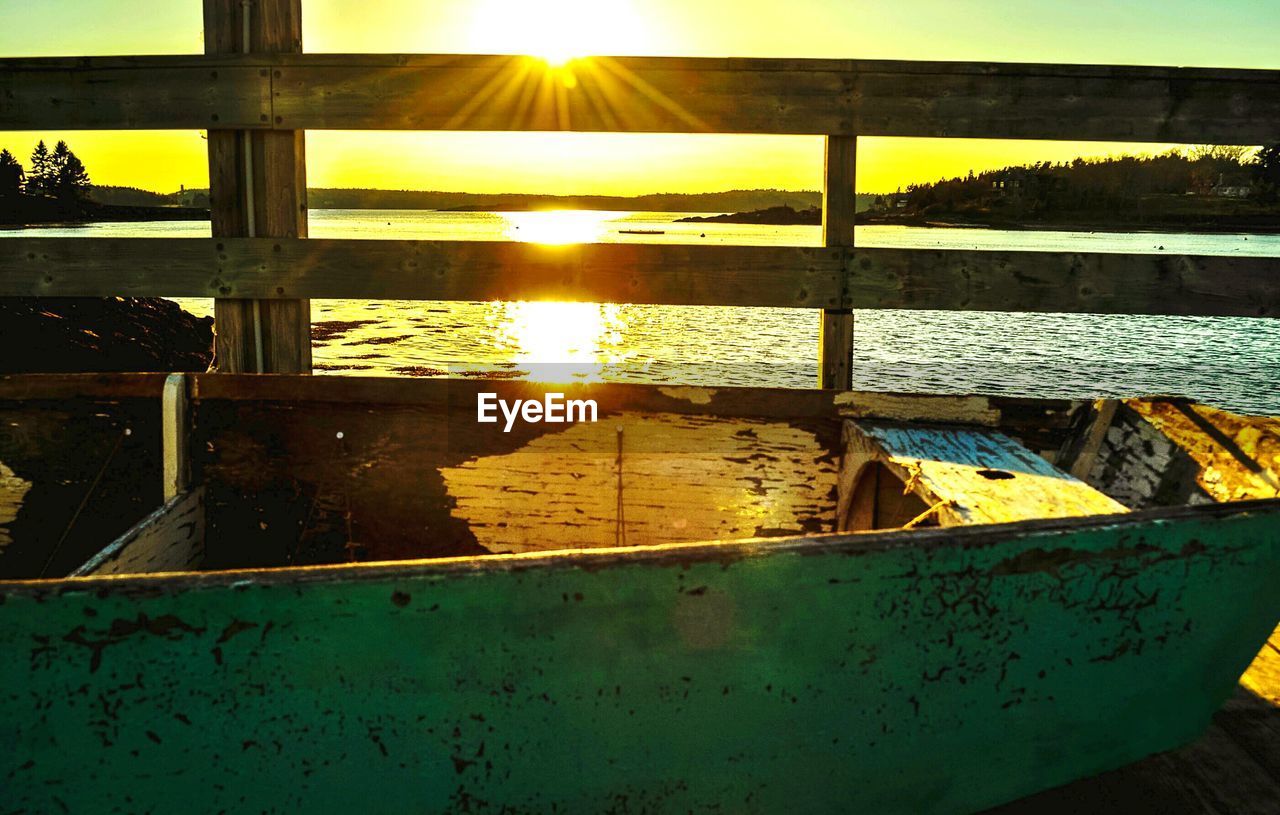 Boat moored by lake against sky during sunset