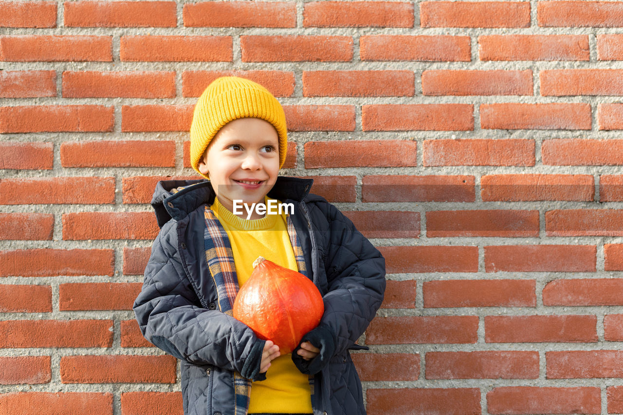 Boy with a pumpkin in his hands against a brick wall.