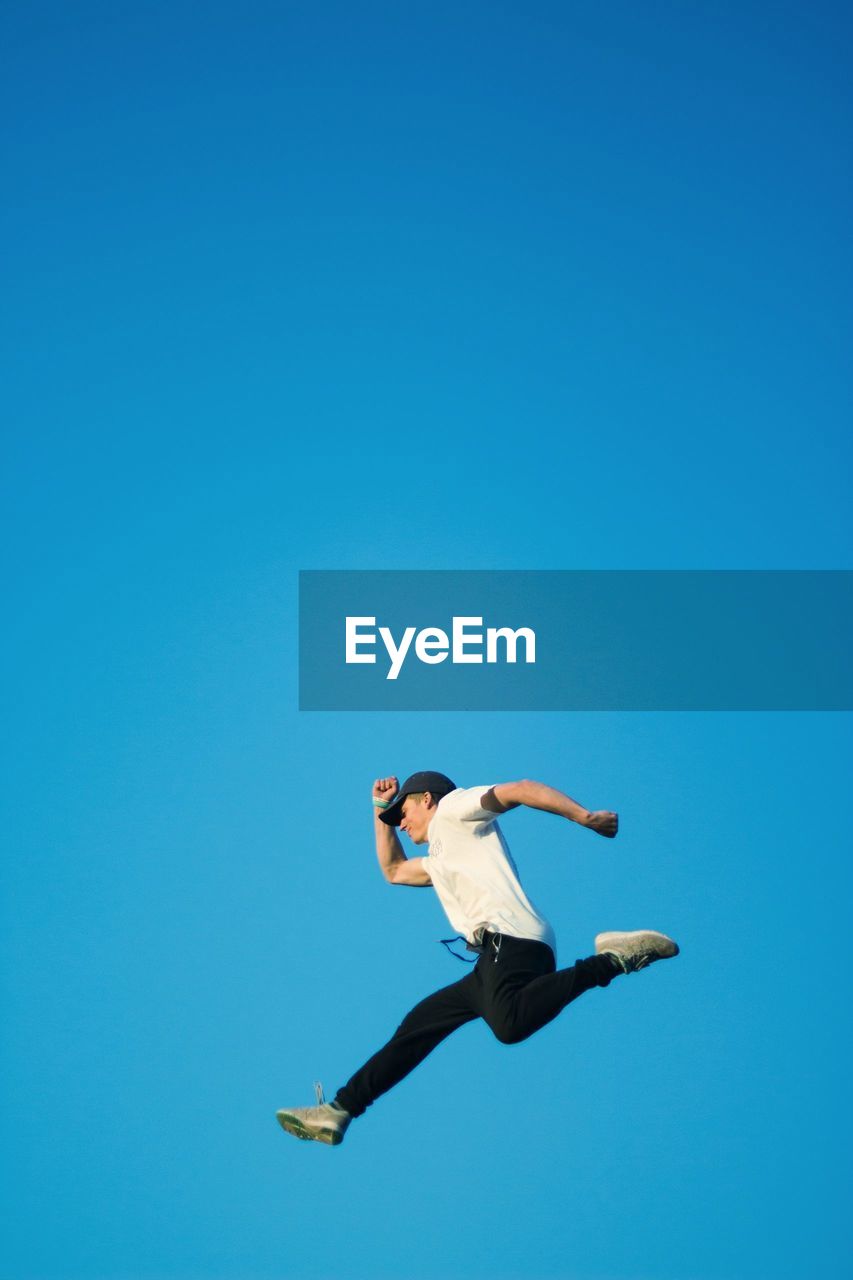 Low angle view of man jumping against clear blue sky