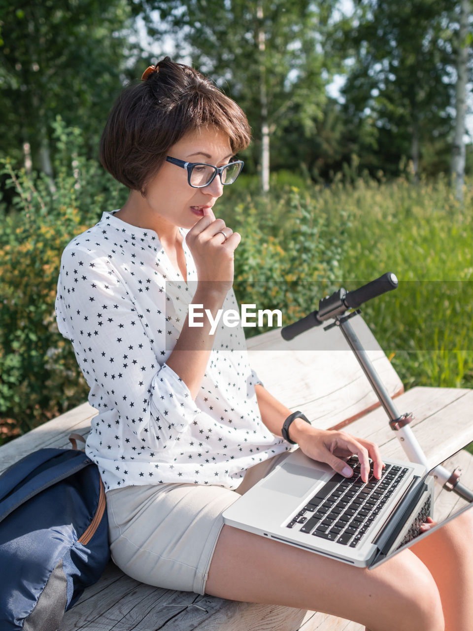 Woman works with laptop on wooden bench in urban park. summer vibes.  workplace for freelancers.