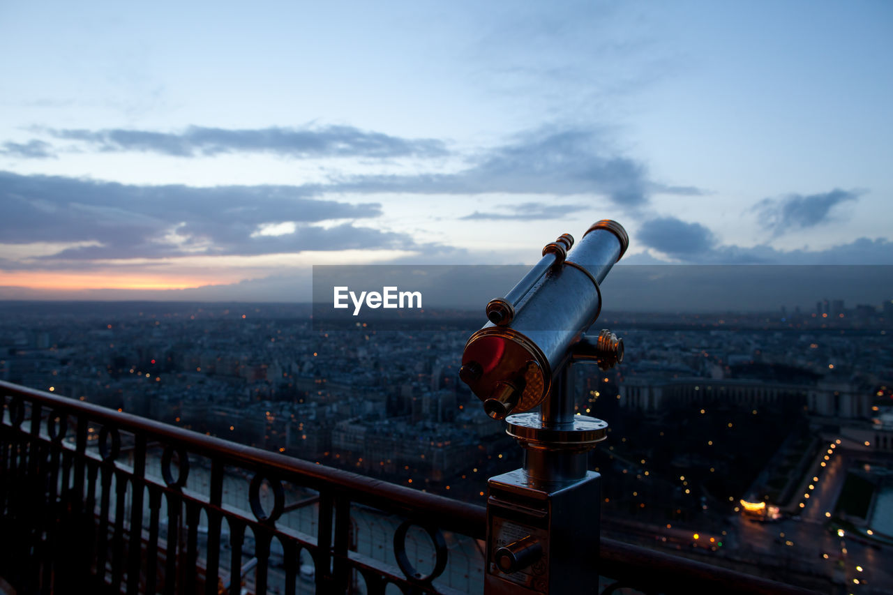 Coin-operated binocular at observation point by cityscape against sky during sunset