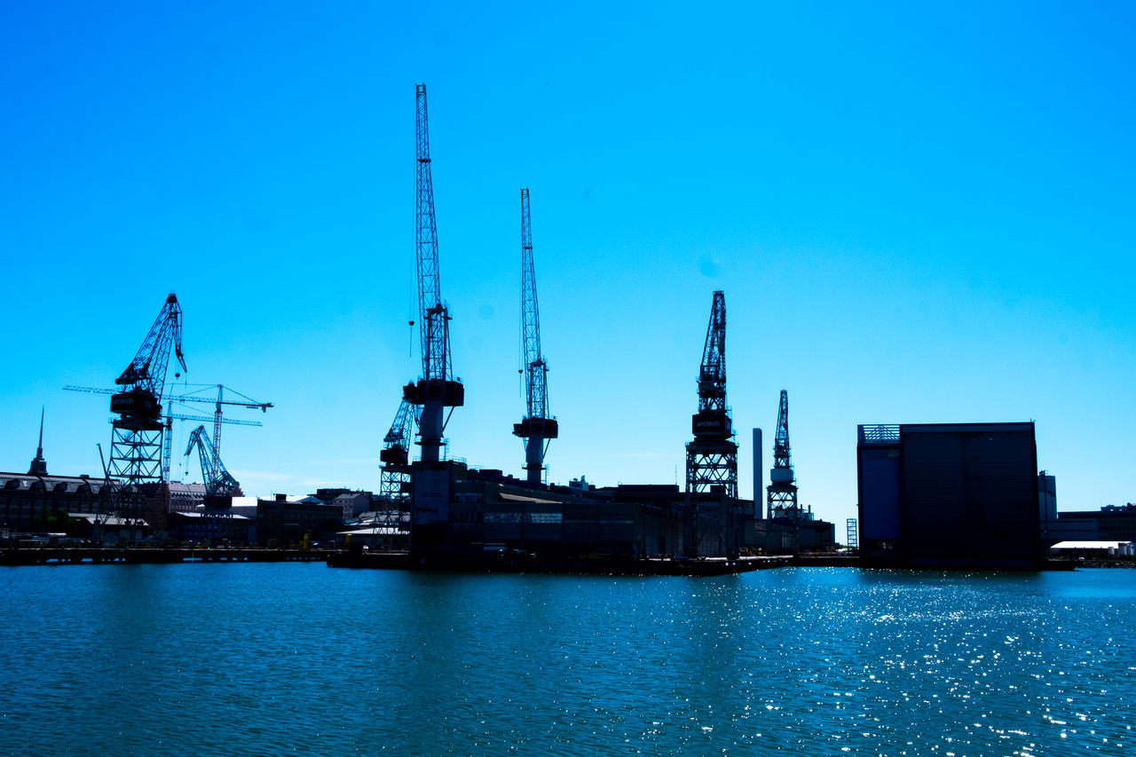 Cranes at commercial dock against blue sky