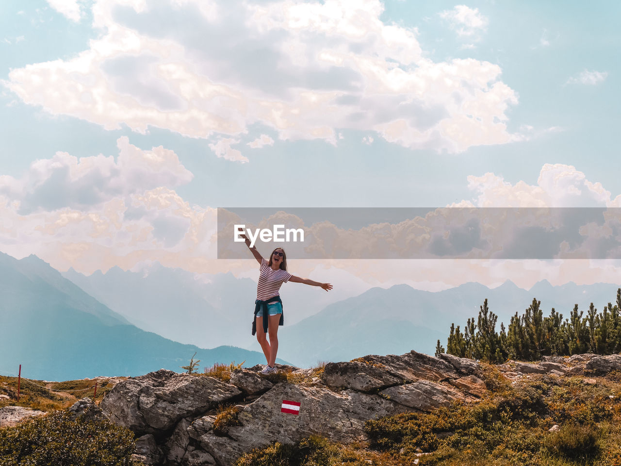 Woman with arms outstretched standing on mountain against sky