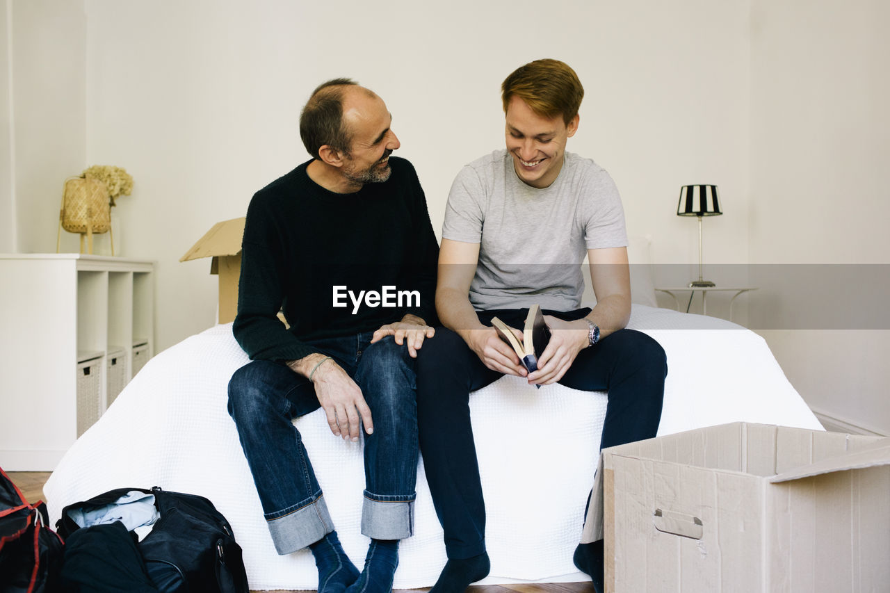 Happy parent talking with son while sitting on bed at home