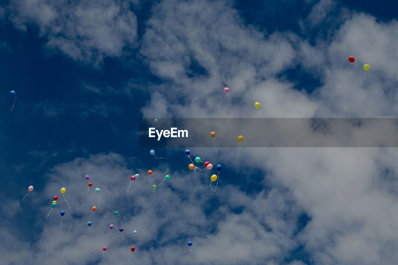 Low angle view of helium balloons flying in cloudy sky