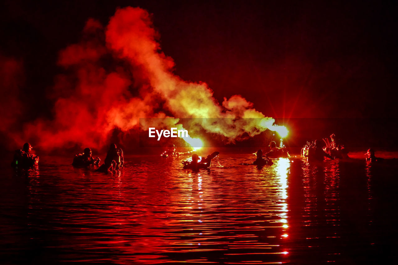 People with distress flare in sea against sky at night