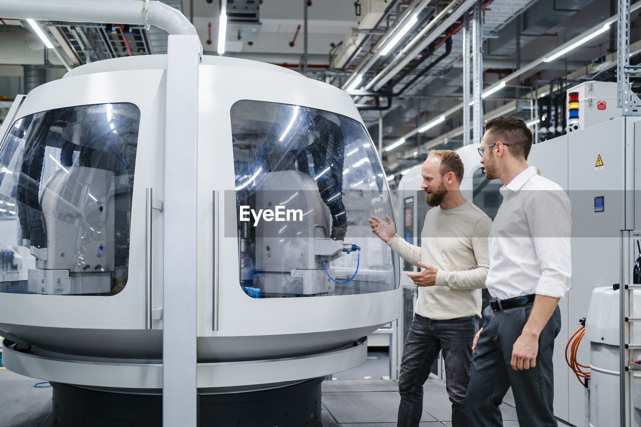 Employee and businessman talking at modern machine in a factory