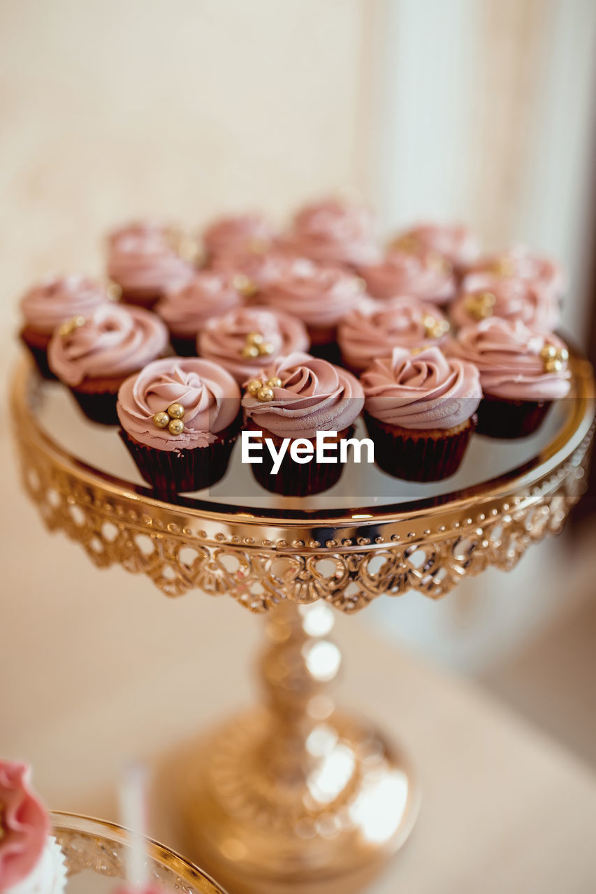 Cupcakes with pink cream and decorated with golden pastry beads on a golden tray 