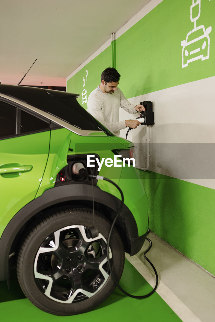 Man plugging cord to charge electric car at charging station