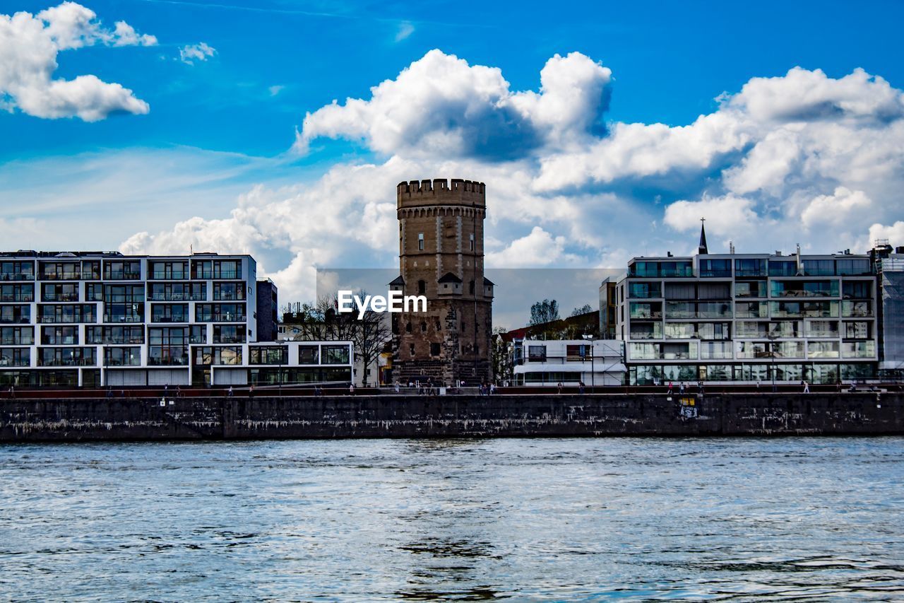 Buildings by river against cloudy sky