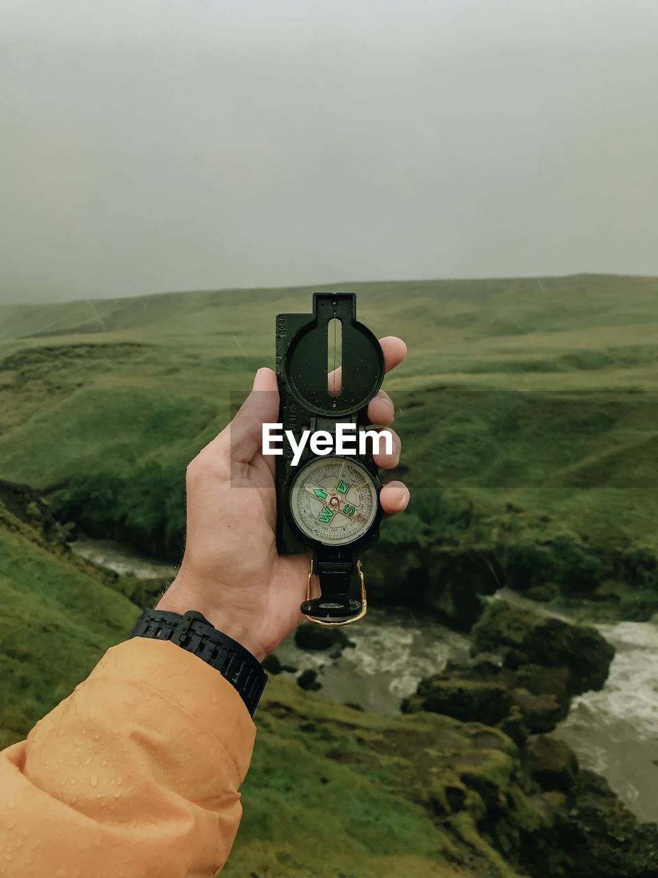 Cropped hand holding navigational compass against landscape