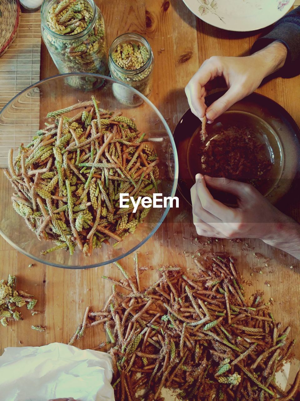 Cropped hands of woman holding pine sprouts over bowl at table