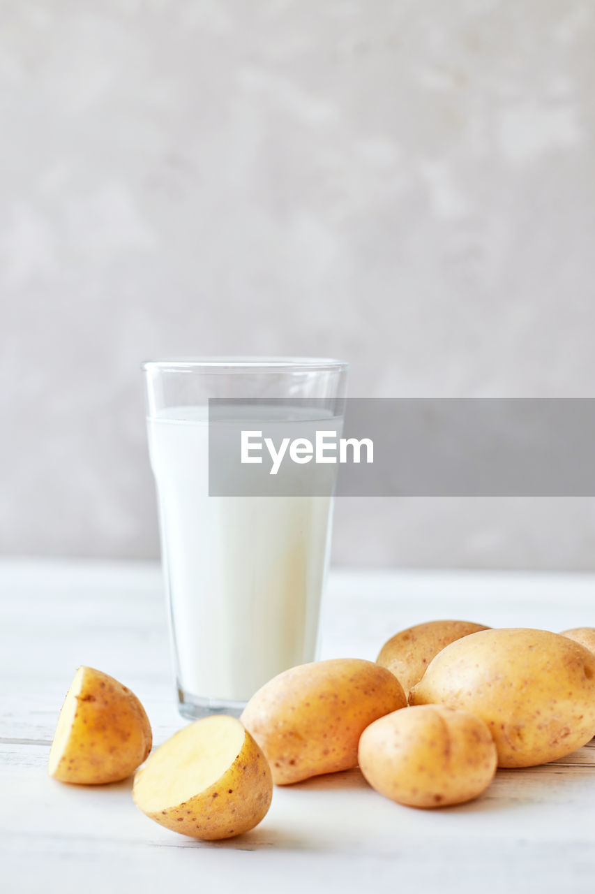 Potato milk in a glass mug stands on the table next to fresh potato tubers. alternative plant milk