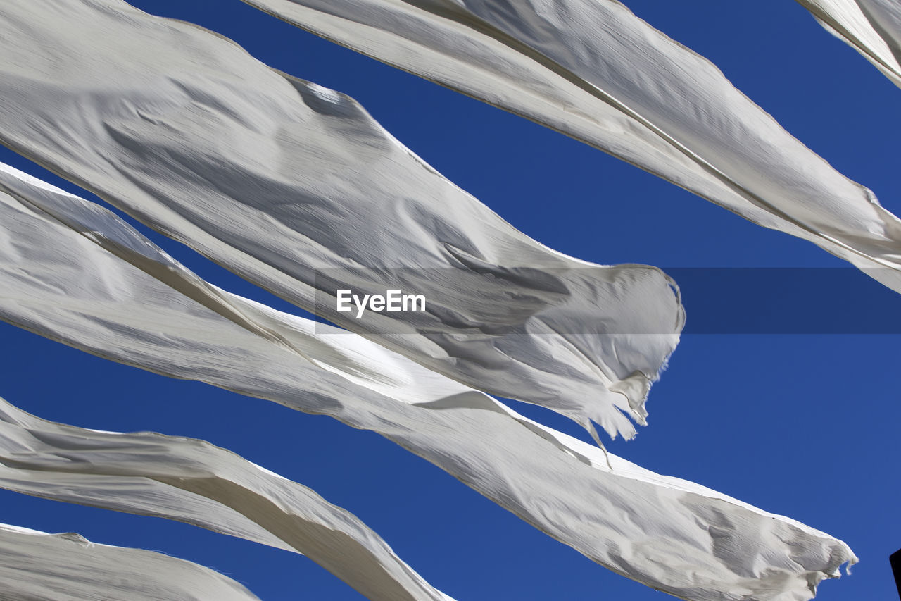 Low angle view of blowing white fabrics against blue sky