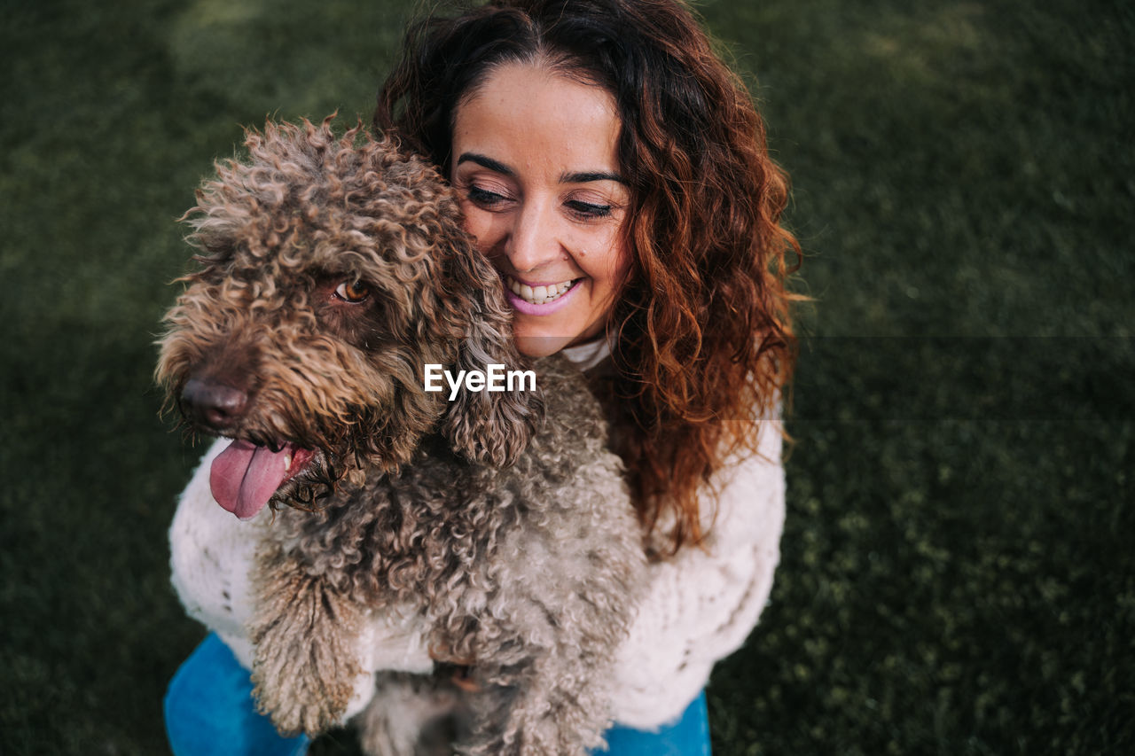 High angle view of smiling woman holding dog on grassy land