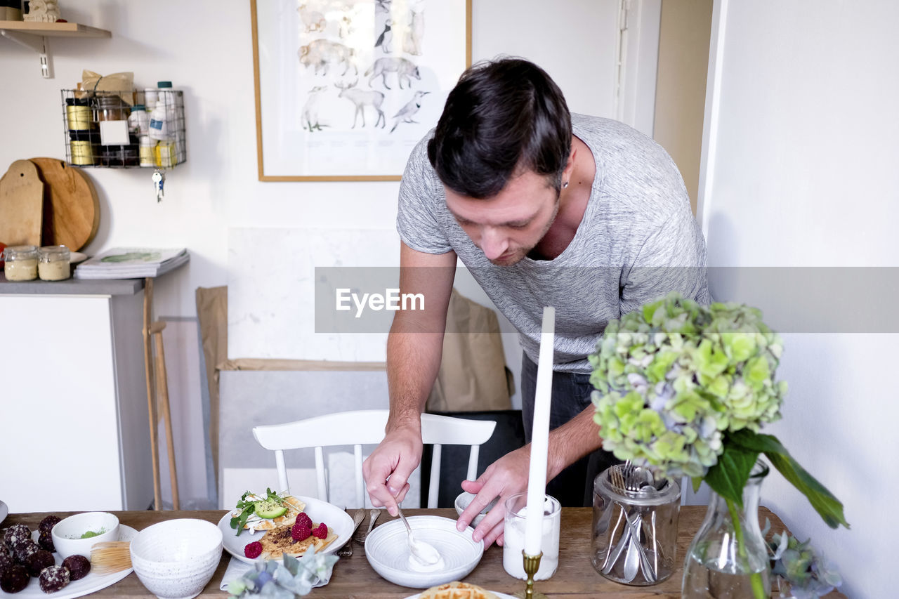 Man spreading yogurt in plate on table at home