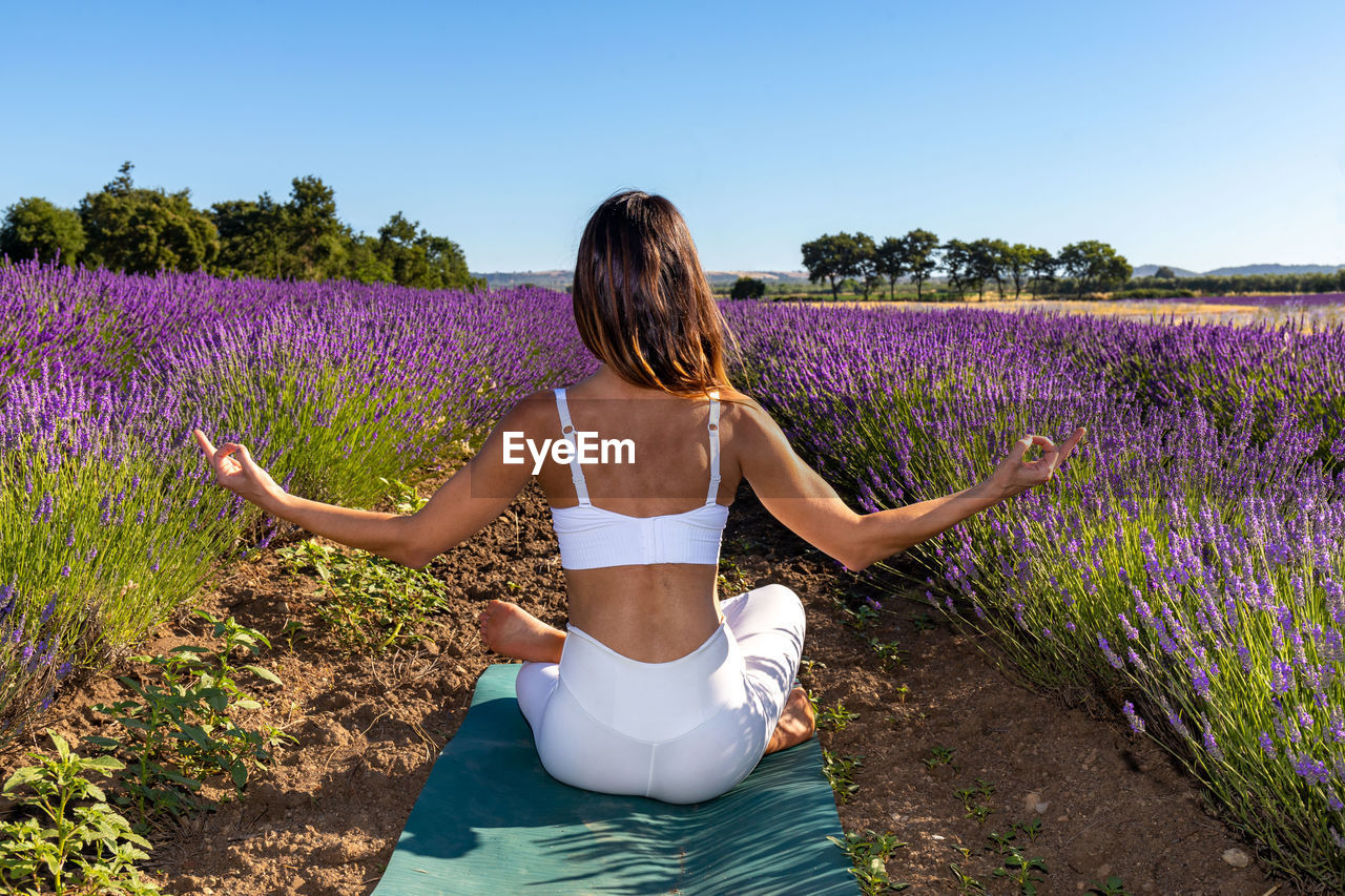 A woman in a white outfit doing meditation yoga in a lavender field.